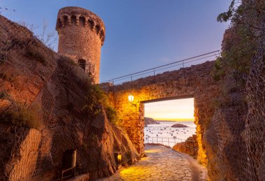 Gündoğumunda İspanya 'nın Girona şehrinde bulunan Akdeniz manzaralı Tossa de Mar Kalesi' nin bir kule ve taş kapısının manzarası.