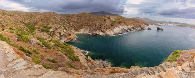 Panoramic view of Cala Jugadora bay near Cadaques showing rocky cliffs surrounding a quiet turquoise bay on a cloudy day, Spain, Catalonia clipart