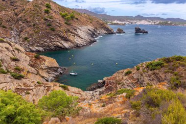 Kadavra yakınlarındaki Cala Jugadora körfezinin manzarası bulutlu bir günde sakin bir turkuaz koyu çevreleyen engebeli uçurumları gösteriyor, İspanya Katalonya