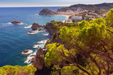 İspanya 'nın Tossa de Mar körfezi ve kıyı şeridinin panoramik manzarasında kayalık uçurumlar, yemyeşil çam ağaçları ve Akdeniz yer almaktadır.