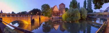 Panoramic view of the historic Weinstadel building and Henkersteg wooden bridge reflecting in the Pegnitz River during dawn in Nuremberg, Germany clipart