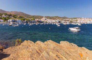 Kadavra limanının manzarası yamaçtaki beyaz boyalı binaları gösteriyor, suda geleneksel balıkçı tekneleri ve açık mavi gökyüzü, İspanya, Katalonya