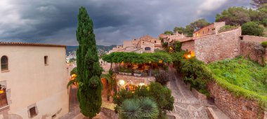Tossa de Mar, İspanya 'nın tarihi Vila Vella bölgesindeki kaldırım taşından caddelerin, taş binaların ve yemyeşil çimlerin manzarası.