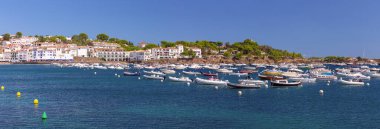 Kadavra limanının manzarası yamaçtaki beyaz boyalı binaları gösteriyor, suda geleneksel balıkçı tekneleri ve açık mavi gökyüzü, İspanya, Katalonya