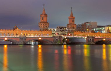 Berlin 'deki Spree Nehri üzerindeki Oberbaum Köprüsü bulutlu gökyüzü ile gün batımında ele geçirildi