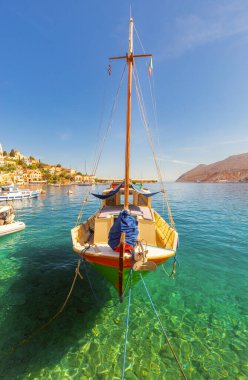 Yunanistan 'ın Symi kentindeki sakin liman sularına demirlemiş renkli balıkçı teknesi, yamaçta geleneksel evleri bulunuyor