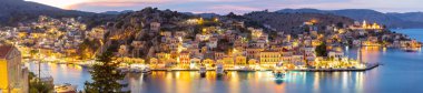 Yunanistan 'ın Symi kentinde alacakaranlıkta aydınlık liman ve tepe evlerinin panoramik manzarası