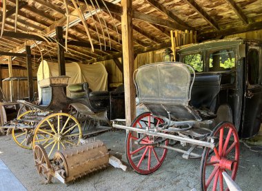 Historic carriage house interior in the recreated and restored 1800 Pioneer Village at Spring Mill State Park, near Mitchell, Indiana with wagons and carriages. clipart