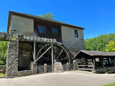 :  Mitchell, Indiana yakınlarındaki Spring Mill State Park 'ta yeniden inşa edilmiş ve restore edilmiş 1800 Pioneer Village' daki tarihi değirmen ve değirmen mavi gökyüzü ve asfalt yol fotokopi alanı..