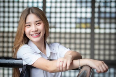 Beautiful young Asian student wearing a Thai university uniform and teething retainer stands smiling cutely in the building during free time while waiting for class.