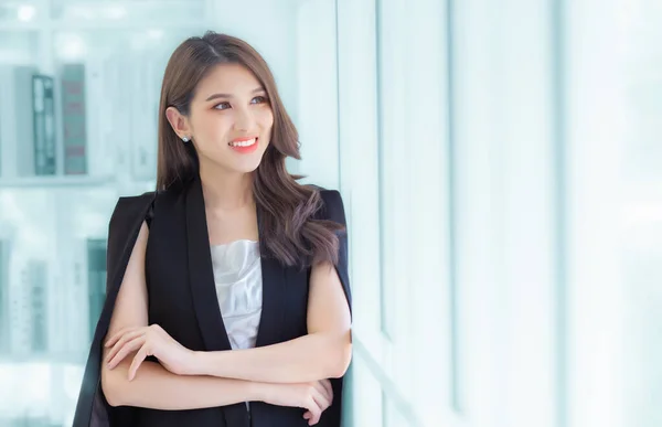Work from home. Professional business Asian young office lady is standing crossed arms looking out the window confident and smiling at work happily.