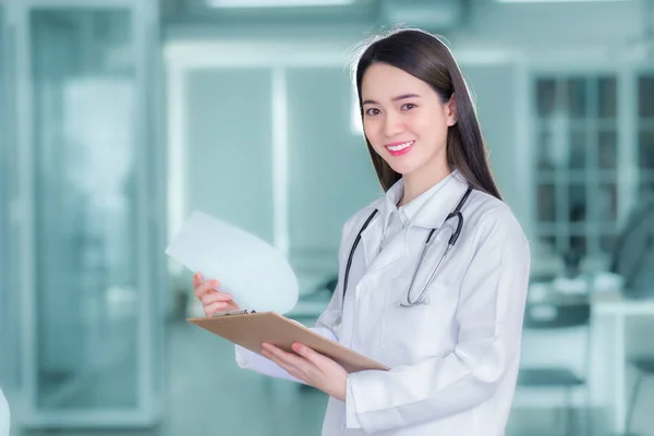 若いプロのアジア女性医師は 次の治療を計画する患者の報告書を検討します 彼女は病院で働いている間にカメラとクリップボードを見て — ストック写真