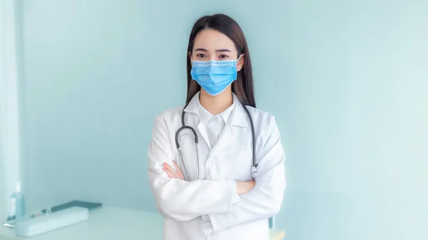 専門的な若いアジアの女性医師は 病院での検査を待つためにオフィスで白いラボコートと聴診器を身に着けています 彼女は呼吸器系に入るコロナウイルスや微生物を保護するために外科用マスクを身に着けています — ストック写真