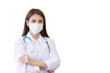 Genç, profesyonel Asyalı kadın doktor, beyaz laboratuvar önlüğü ve yüz maskesi giyerken kendine güvenerek ayakta duruyor ve gülümsüyor..