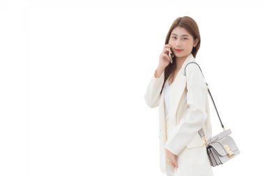 Beyaz takım elbiseli, genç ve güzel Asyalı profesyonel çalışan kadın gülümser ve mutlu bir iş gününde akıllı telefonu elinde tutarken izole beyaz bir arka plan kullanır..