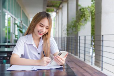 Akıllı telefon kullanarak ve iş hakkında bir şeyler yazarak genç Asyalı kız öğrenci. Masaya bir sürü belge koydu. Üniversitede bilgi aramak için çalışırken gülümsedi..
