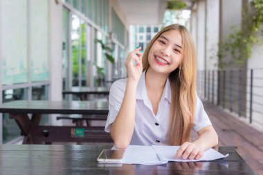 Yetişkin Taylandlı öğrencinin portresi. Üniformalı güzel Asyalı kız öğrenci kampüs üniversitesinin dışında çalışırken kameraya bakıp gülümsüyor..