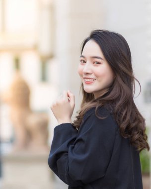 Dikey 4: 5 'te, siyah bornozlu, şık Asyalı bir kadın şehirde yürürken, gülümseyip, dışarıdaki kameralara bakarken, modern şehir yaşam tarzı ve moda portresi.