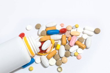 Masada bir sürü hap var, yakın plan. Tabletler farklı şekiller ve renkler masaya saçılmış. Haplar şişeden döküldü.