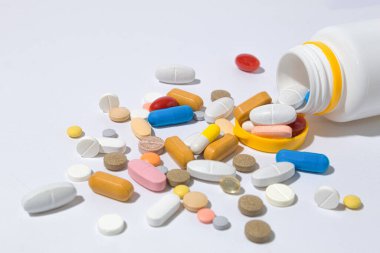 Masada bir sürü hap var, yakın plan. Tabletler farklı şekiller ve renkler masaya saçılmış. Haplar şişeden döküldü.