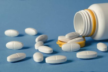 Masaya saçılmış beyaz renkli haplar, yakın plan. Masada kapsül şeklinde bir sürü hap var. Haplar şişeden döküldü. Boşluğu kopyala