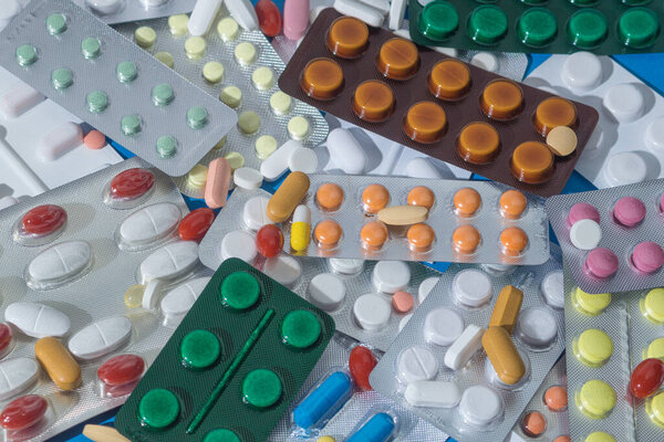 A large pile of pills in bundles scattered on the table. A mound of multi-colored tablets and blister packs. Close-up, copy space
