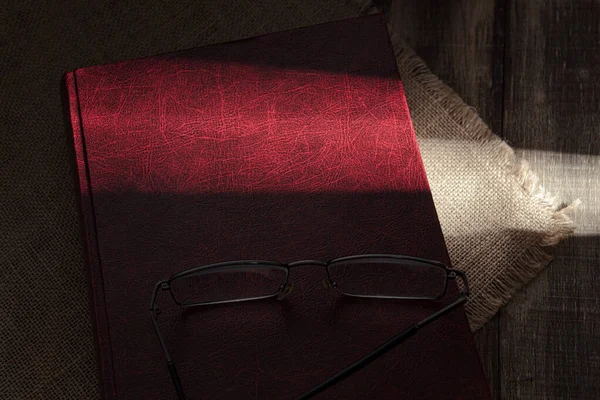 A hard ray of sun falls on an old red book. Sunbeam in the dark, on a book. Close-up. Old red book