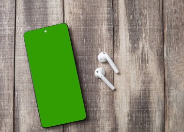 Cep telefonu ve kulaklıklar, yakın plan. Kromakey. Uzayı kopyala Modern kulaklıkları taşınabilir telefon kılıfında kapat.