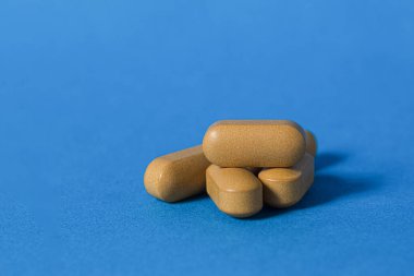 Mavi arka planda kahverengi haplar. Yakın plan. Tablet kapsülleri, tıbbi ve beslenme takviyeleri. Boşluğu kopyala