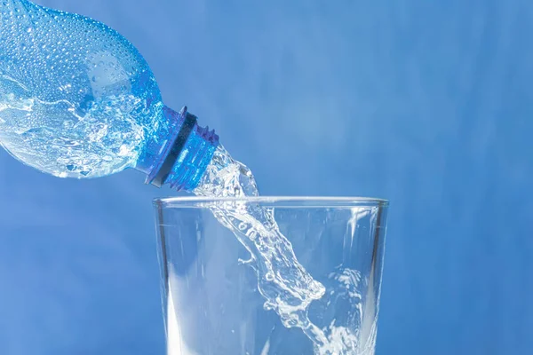 stock image Fresh and cool water flows from the neck of the bottle. Water is poured from a plastic bottle into a glass. Copy space. Close-up