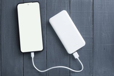 Telefon ve elektrik bankası, ahşap bir arka planda. Uzayı kopyala Beyaz enerji bankası ve ahşap arka planda akıllı telefon. Metin için boşluk olan beyaz telefon ekranı