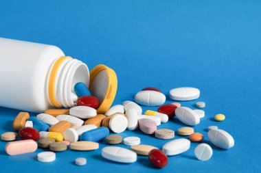 Plastik şişeden bir sürü hap döküldü. Mavi arka planda plastik bir şişeden dökülen çok renkli haplar. Çeşitli ilaç ve haplar. Tıbbi konsept. Boşluğu kopyala