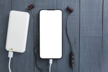 Telefon ve elektrik bankası, ahşap bir arka planda. Uzayı kopyala Beyaz enerji bankası ve ahşap arka planda akıllı telefon. Metin için boşluk olan beyaz telefon ekranı