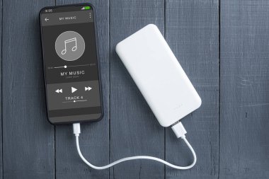 Telefon ve elektrik bankası, ahşap bir arka planda. Uzayı kopyala Beyaz enerji bankası ve ahşap arka planda akıllı telefon. Metin için boşluk olan beyaz telefon ekranı