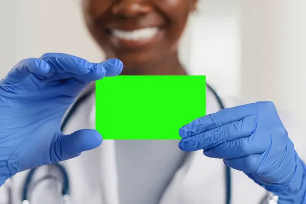 The doctor is holding a business card, his hands are in medical gloves. The doctor shows his business card, chroma key. Copy space