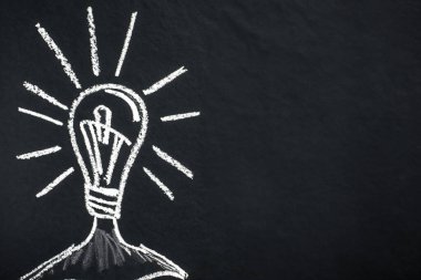 Kavramsal fikir. Karanlık bir tahtaya tebeşirle bir ampul çizilir. Koyu dokulu arka planda beyaz ampul, uzayı kopyala. Görüntü