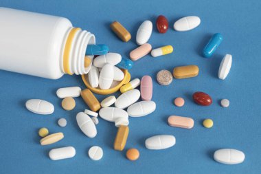 Beyaz haplar, beyaz bir şişeden dağılmış kapsüller, mavi arka planda bir kavanoz. Sağlık ve tedavi konsepti. Web Afişi