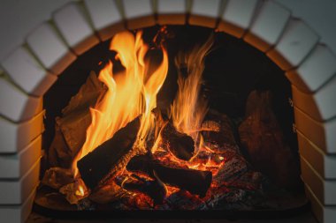 Şömine çok güzel yanıyor. Yanan odun ve alevler, karanlık bir arka planda, yakın plan. Tahtalardan yapılmış büyük bir şenlik ateşi. Parlak alevler içinde yakacak odun.
