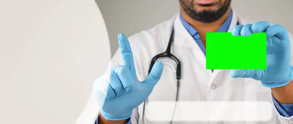 The doctor is holding a business card, his hands are in medical gloves. The doctor shows his business card, chroma key. Copy space