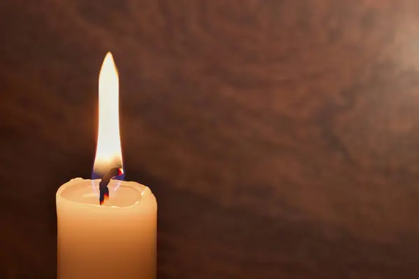 A candle burns on a dark background. Enlarged image of a candle in the dark. It burns and symbolizes grief and mourning. Background with copy space