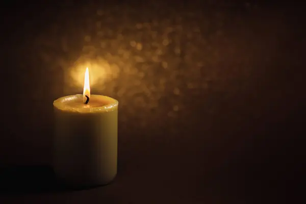 A wax candle is burning on a dark background. Flame of one candle at night close-up. Copy space.