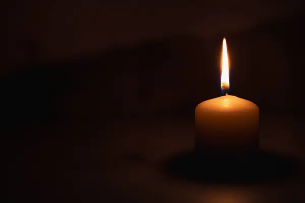 A wax candle is burning on a dark background. Flame of one candle at night close-up. Copy space.
