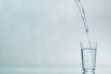 Cam bir deney şişesi suyla doludur. Bir bardağı suyla doldurma süreci. Mavi arka plandaki bir bardağa su dökmek. Boşluğu kopyala.