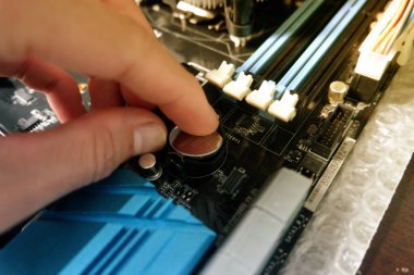 Bir adamın elleri bilgisayar ana kartının BIOS bataryasını değiştiriyor..
