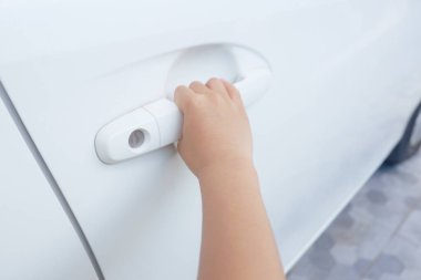 Bir çocuğun eli beyaz bir arabanın kapısını açmak için jest yapıyor..