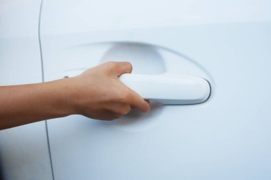 Bir çocuğun eli kapıyı açmak için beyaz arabanın kapı kolunu tutuyor..