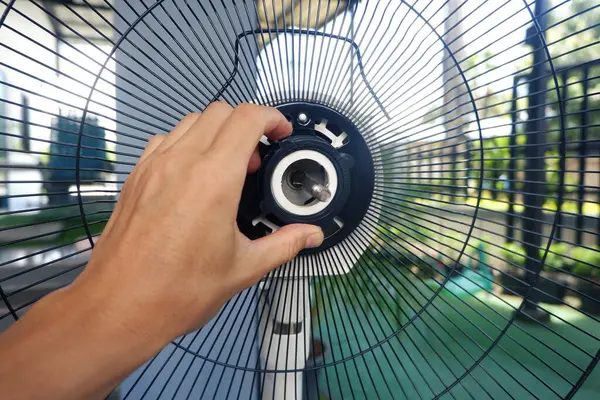 Bir teknisyenin elleri vantilatörü tamir eder, kondansatörleri değiştirir, termal sigortaları kontrol eder ve vantilatör ızgarasını monte eder..