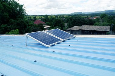 Kırsal bir evin mavi metal çatısına iki büyük güneş paneli monte edilir. Onları desteklemek için çelik bacaklar kullanılır..