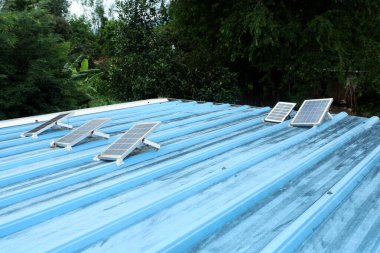 Kırsal bir evin mavi metal çatısına kurulmuş küçük güneş panelleri.
