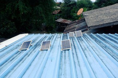 Kırsal bir evin mavi metal çatısına kurulmuş küçük güneş panelleri.